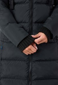 Giacca a vento nera con texture trapuntata, dotata di chiusura a zip e polsini neri a coste. Decorata con una piccola bandiera svedese.