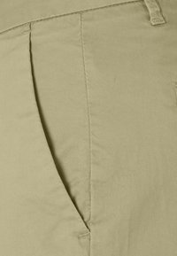 Khaki tygbyxor med en slät textur, standard passform och diskret sidofickdetaljering. Enkla, rena linjer med en neutral färg.