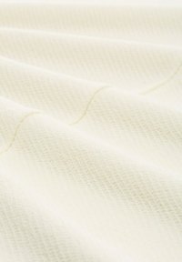 Roomkleurig textiel met een subtiele ruitpatroon, met zachte golven en zichtbare stiksels voor extra detail.