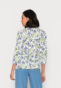 Blusa floral com padrões azuis e verdes sobre um fundo branco, com mangas de três quartos e um design com cintura ajustada.