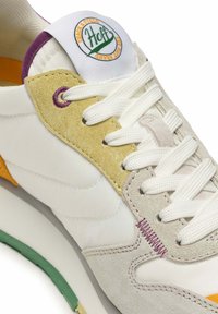 White sneaker with suede overlays in yellow, grey, and orange. Features white laces, stitched accents, and a logo patch on the tongue.