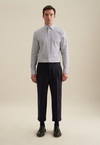 Een button-up shirt met een klein marineblauw en wit ruitpatroon, gedragen met donkere op maat gemaakte broeken en zwarte leren schoenen. Glad materiaal en gestructureerde pasvorm.
