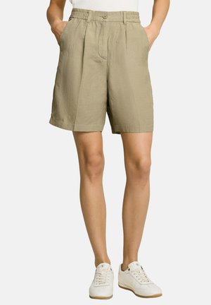 Beige knielange Shorts mit Knopf und elastischem Bund, Seitentaschen, getragen mit weißen Sneakers und weißem Oberteil.