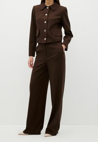 Brun kort kavaj med stor krage, sex knappar och två framfickor, i kombination med matchande vida byxor. Mjuk tygstruktur.