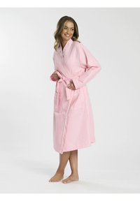 Robe en tricot à mailles rose avec une taille ceinturée, des manches longues, deux poches avant et des détails en passepoil blanc. Design long jusqu'au sol.