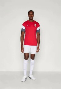 Červený športový dres so šedými a bielymi rukávmi, s logom na hrudi, doplnený bielymi šortkami a zodpovedajúcimi ponožkami.