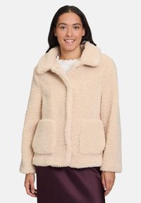 Beżowa kurtka teddy o puszystej fakturze, z dużym kołnierzem i dwiema przednimi kieszeniami, z zapięciem na guziki i luźnym krojem.