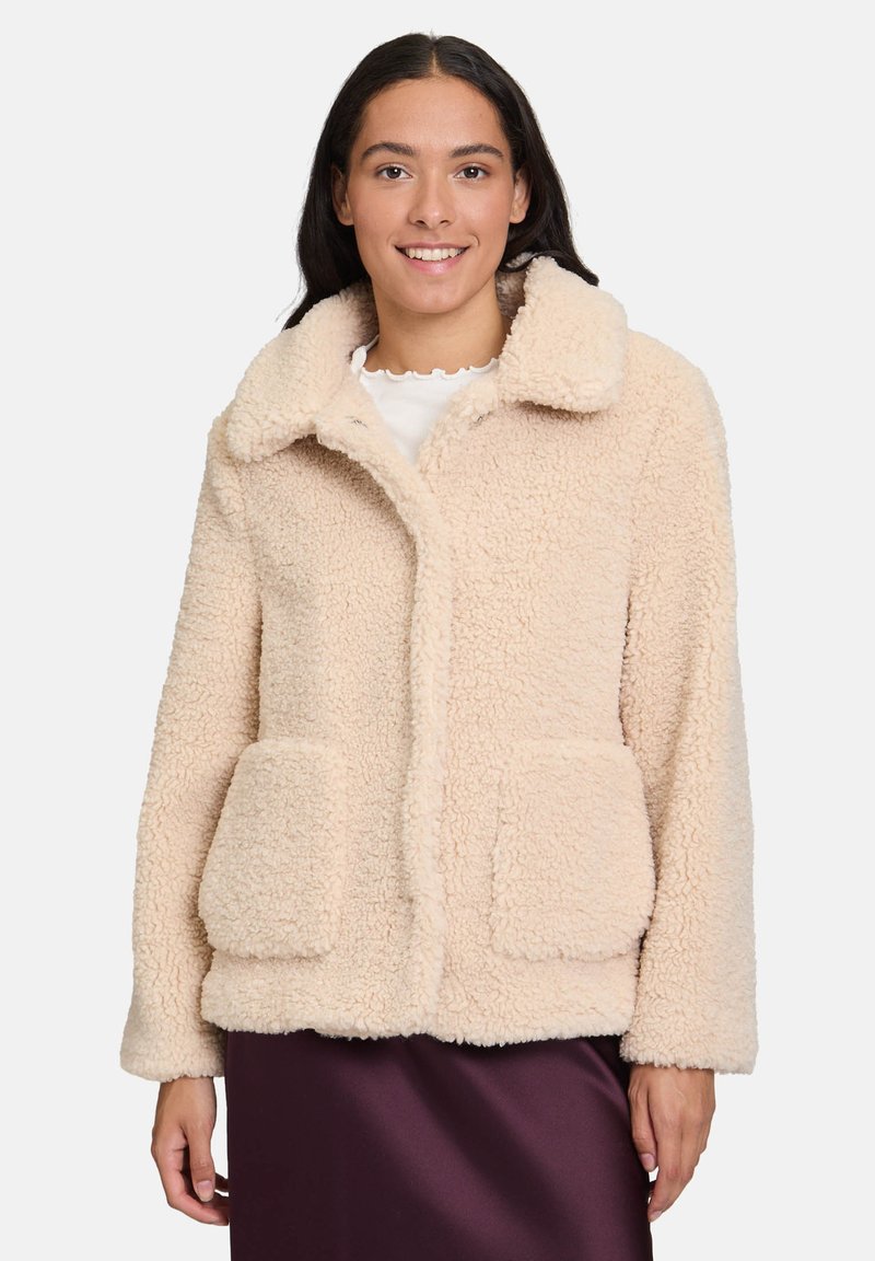 Beżowa kurtka teddy o puszystej fakturze, z dużym kołnierzem i dwiema przednimi kieszeniami, z zapięciem na guziki i luźnym krojem.