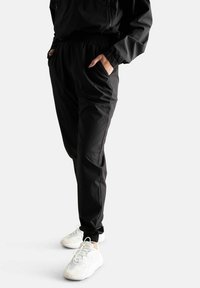 Pantaloni sportivi neri con una cintura elastica, tasche laterali e gamba affusolata, abbinati a scarpe da ginnastica bianche con design testurizzati.