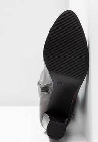 Bottine en cuir noir avec une semelle plate, un fond en caoutchouc texturé, un bout arrondi et un zip sur le côté, posée sur un fond blanc.