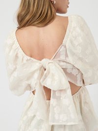 White floral-patterned dress with a back tie, featuring puffy sleeves and a scooped back, made of lightweight, textured fabric.