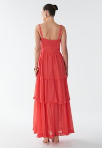 Robe longue corail avec couches superposées, bretelles spaghetti ajustables et ourlet volanté. Tissu lisse et léger, dos élastique.