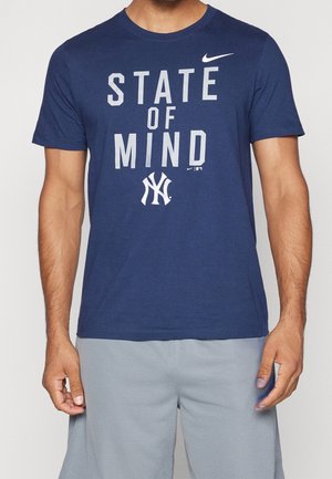 Homme portant un t-shirt Nike bleu marine avec l'inscription "STATE OF MIND" et le logo des New York Yankees, associé à un short gris clair.