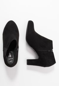 Černé semišové kotníkové boty s špičatou špičkou, postranním zipem a středně vysokým blokovým podpatkem, s hladkou texturou a bez viditelných vzorů.