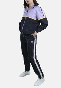 Tuta blu navy e lavanda dallo stile sportivo con dettagli gialli. Presenta strisce laterali bianche e una giacca con zip e tasche.