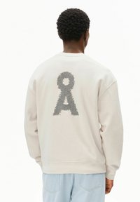 Felpa beige chiaro con un motivo grafico testurizzato in grigio scuro sul retro. Collo a giro e polsini a costine completano il design.