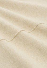 Jasnobeżowa tkanina o teksturowej powierzchni, z subtelnymi falami i detalem przeszycia, podkreślająca miękkość i gładkość.