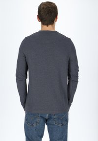 Mörkgrå långärmad tröja med ribbad struktur, rund halsringning och avslappnad passform, kombinerad med blå jeans.