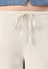 Linnedukser i off-white med strammemansjett i midjen. Teksturen er glatt og litt strukturert, med et naturlig fiberutseende.