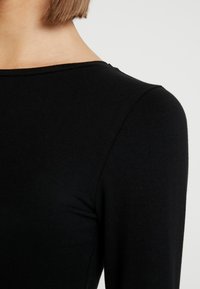 Schwarzes Langarmshirt mit rundem Halsausschnitt. Glatte Textur und figurbetontes Design, das den Schulter- und Halsbereich hervorhebt.