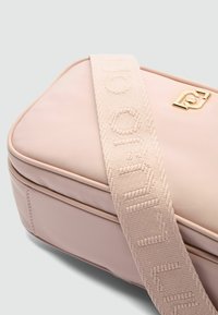 Hellrosa rechteckige Tasche mit glatter Textur, goldfarbenen Beschlägen und einem breiten Riemen mit geprägter Schrift.