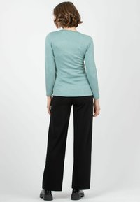 Ljusblå långärmad topp med en figurnära design, kombinerad med högmidjade svarta vida byxor och svarta skor. Helt slät yta.