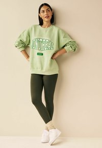 Mintgrøn oversized sweatshirt med "MONTREAL" grafik, parret med mørkegrønne leggings og hvide sneakers. Blødt stof, afslappet pasform.