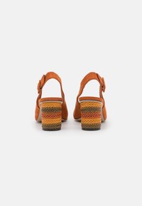 Zapatos slingback de ante naranja con un tacón de bloque texturizado y tejido que presenta patrones a rayas en amarillo, naranja y verde.