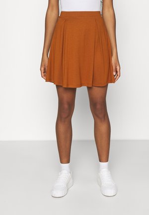 Rust-orange, flagrende nederdel lavet af blød stof med læg ved taljen. Parret med hvide sneakers og sokker for kontrast.