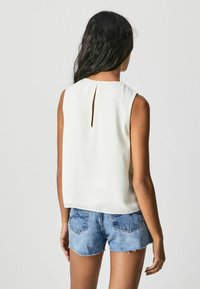 Hvid ærmeløs bluse med en nøglehul-ryg, lavet af glat materiale. Sammen med denimshorts med frayed kanter og baglommer.
