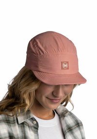 Gorra de tela rosa con un pico estructurado, que presenta un parche rectangular con un logo naranja. El material parece ligero y texturizado, con detalles de costura.