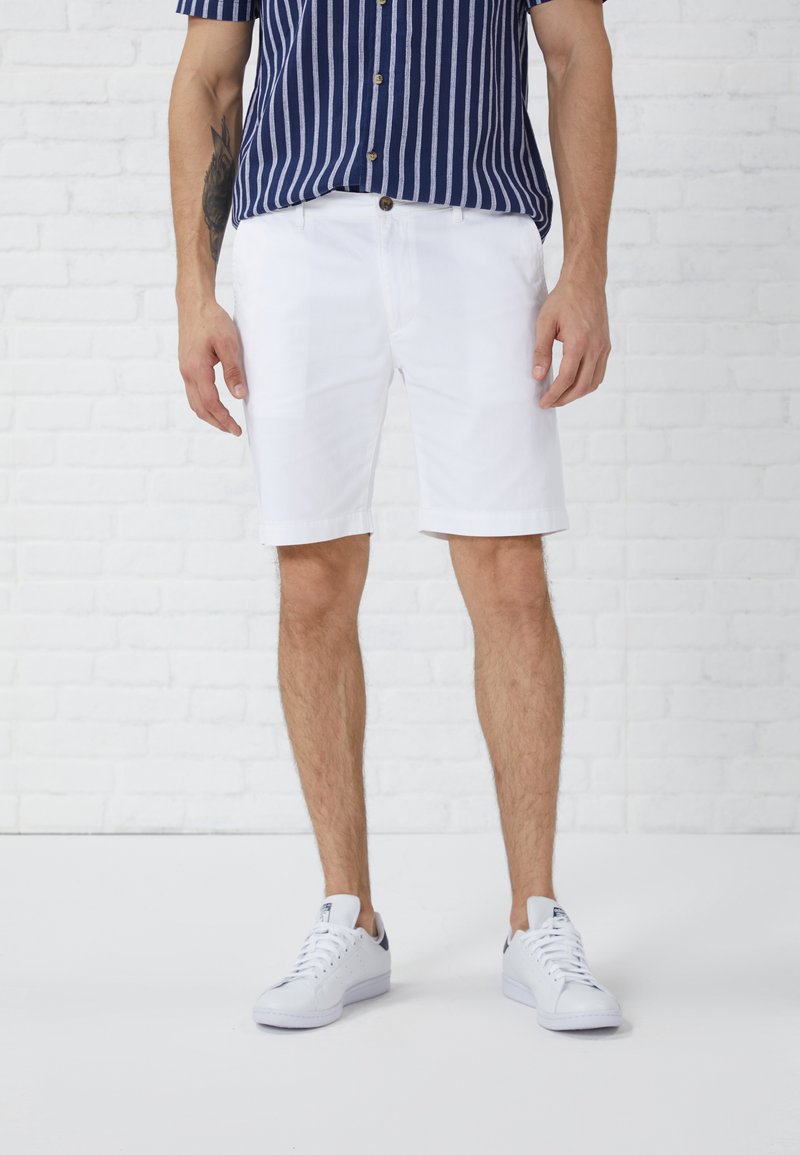 Shorts blancs avec un devant plat et des jambes droites, associés à une chemise à rayures bleu marine et à des baskets blanches. Texture de tissu lisse.