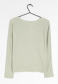 Jasnozielona bluzka z długim rękawem, zaokrąglonym dekoltem i poziomą fakturą prążkowaną. Zawieszona na czarnym haczyku.
