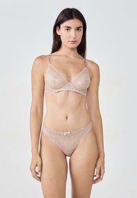 Spitzenunterwäsche-Set in hellem Beige, bestehend aus einem dreieckigen Bralette mit gewellten Kanten und einem passenden Thong mit einer kleinen Schleifenverzierung.