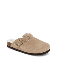 Zoccoli in suede tan con un interno peloso, cinturino regolabile e suola in gomma texturizzata. Forma sagomata con dettagli di design minimi.