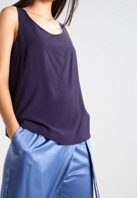 Mörkblå ärmlös topp i slät tyg, med rundad halsringning och en avslappnad passform, matchad med glänsande ljusblå byxor.