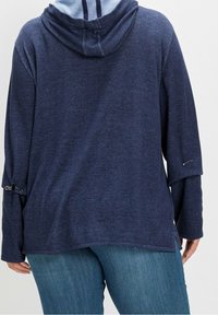 Marineblaues Kapuzensweatshirt mit strukturiertem Finish, bietet eine lockere Passform, überschnittene Schultern und silberne Hardware-Details an den Ärmeln.