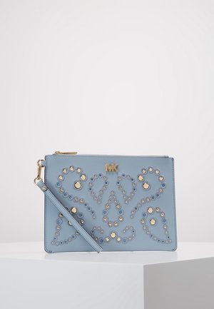 Bolso de mano azul claro con tachuelas doradas circulares y ovaladas en patrones simétricos y logo dorado "MK" en la parte delantera.