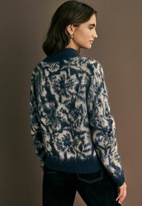 Marineblauer und cremefarbener gemusterter Pullover mit strukturiertem Strick, rundem Ausschnitt und gerippter Säume. Er hat einen lockeren Schnitt und lange Ärmel.