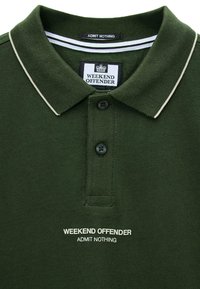 Tmavě zelené polo tričko s bílým lemem na límci, se dvěma knoflíky a bílým textem "WEEKEND OFFENDER ADMIT NOTHING" pod knoflíky.