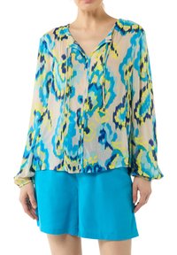Leichte Bluse mit langen Ärmeln und einem mehrfarbigen, abstrakten Muster in Blau, Gelb und Grün. Besitzt eine Knopfleiste und einen Kordelzug am Ausschnitt.