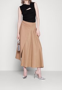 Top senza maniche aderente nero con dettaglio intrecciato, abbinato a una gonna midi plissettata beige e scarpe con tacco alto argentate. Piccola borsa decorata come accessorio.