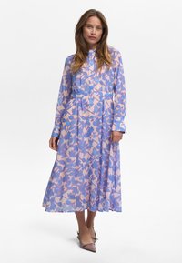 Robe longue à boutonner en tissu léger avec un motif floral pastel en rose et bleu, dotée de manches longues et d'une ceinture à la taille.