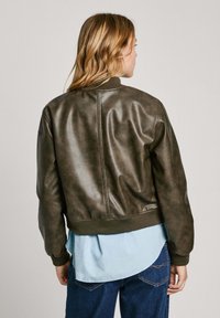 Bruine leren bomberjack met ribgebreide mouwen en onderrand; heeft een gladde textuur en een aansluitend ontwerp. Draag over een lichtblauw shirt.