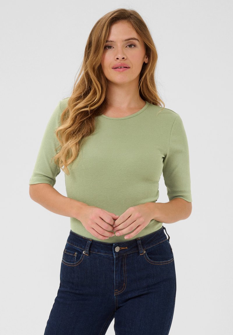 Haut en tricot côtelé vert avec un col rond et des manches à longueur de coude, associé à un jean taille haute bleu foncé avec poches et bouton.