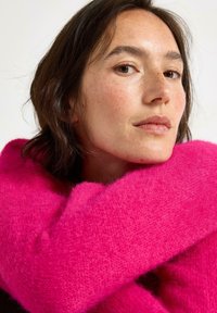 Lys pink, fluffy sweater viklet omkring modelens hals, med en blød tekstur og et hyggeligt design.
