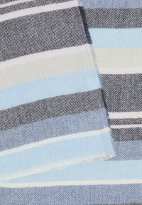Textile tissé en différentes nuances de bleu, gris et des rayures blanches. Présente une texture douce avec des bords à franges et un motif en chevrons subtil.
