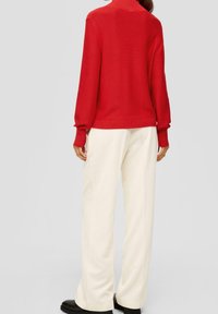 Roter Strickpullover mit hohem Kragen, gerippten Bündchen, kombiniert mit cremefarbenen, strukturierten, weit geschnittenen Hosen und schwarzen Schuhen. Einfaches und lässiges Design.