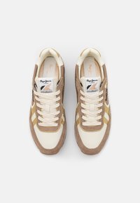 Baskets en cuir crème avec des accents en daim marron clair et des détails beiges. Elles présentent une fermeture à lacets plats et une languette avec logo.