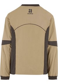Beige jacket with brown accents, featuring a round yoke design and ribbed collar. Made from lightweight fabric with a smooth texture.